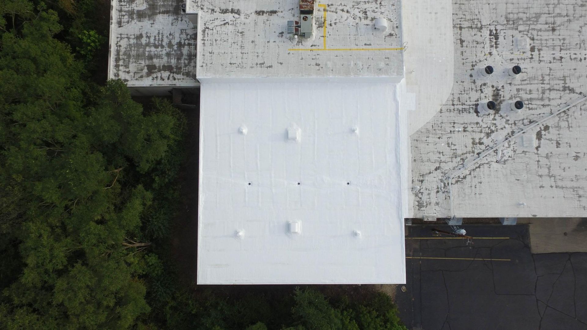 An aerial view of a white roof of a building surrounded by trees.