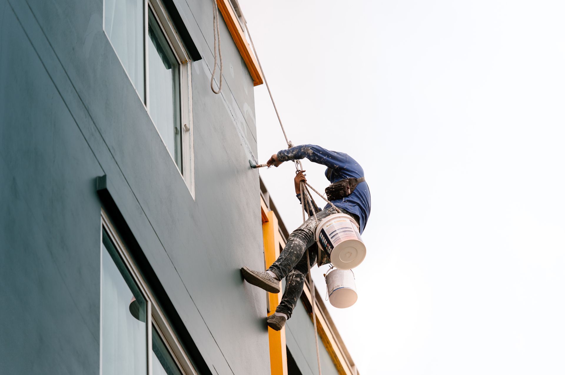 Window cleaners rappelling down a tall gray building with buckets and harnesses
