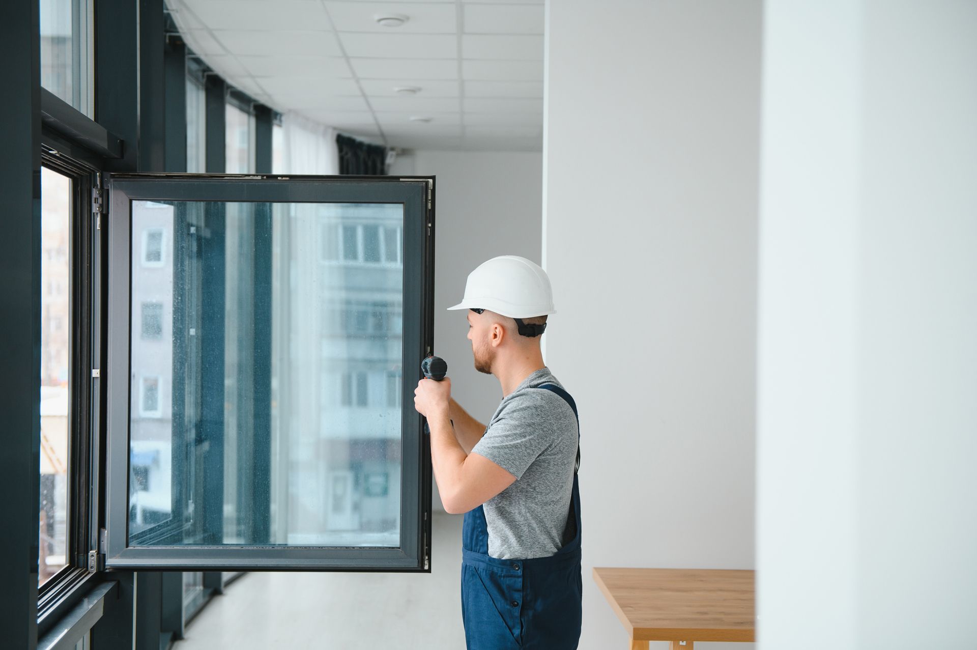 Worker in a hard hat inspecting a large open window in a bright room