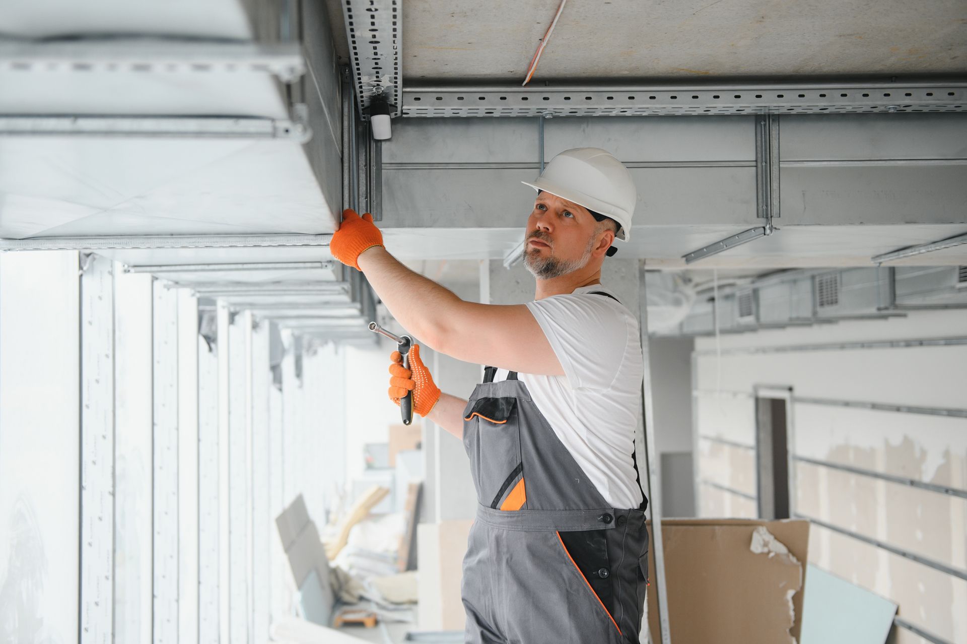 Construction worker adjusting a ceiling beam in a white interior under renovation
