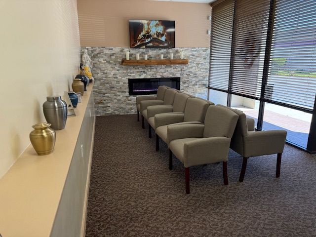 A waiting area with beige armchairs, a stone wall with a fireplace, and urns on a shelf along the wall.