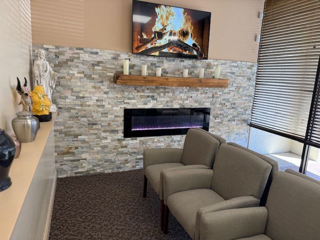 A waiting room featuring a stone accent wall, a fireplace, a mounted television, and beige armchairs.