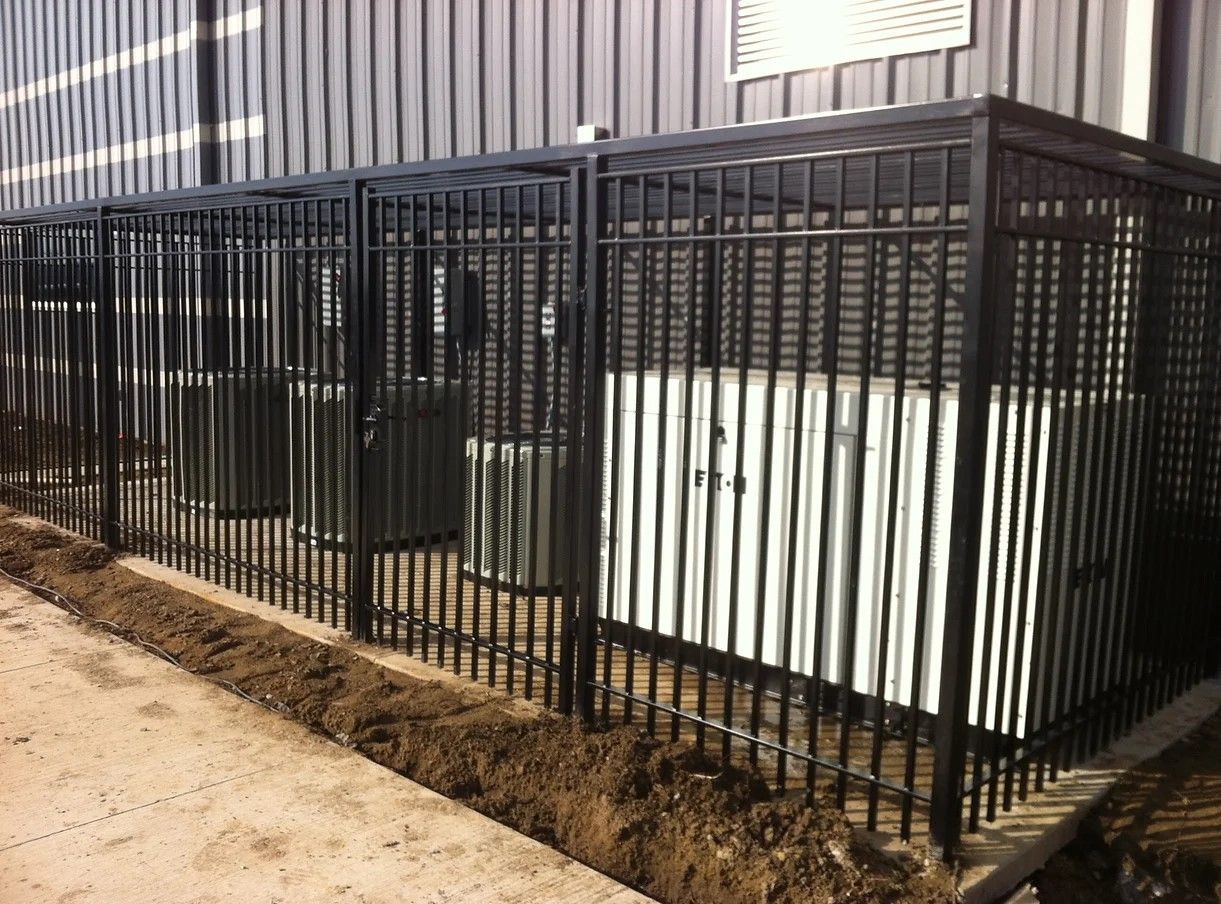 A metal fence surrounds a building with air conditioners behind it