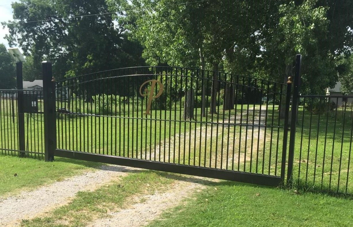 A wrought iron fence surrounds a grassy field with trees in the background.