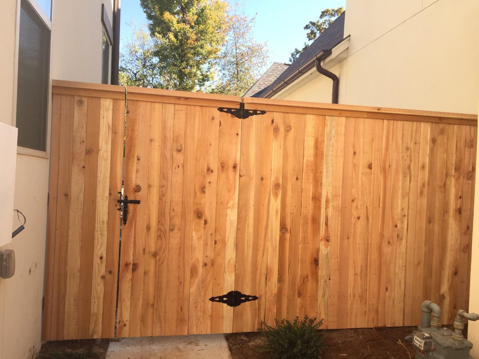 A wooden fence with a black door is in front of a house.