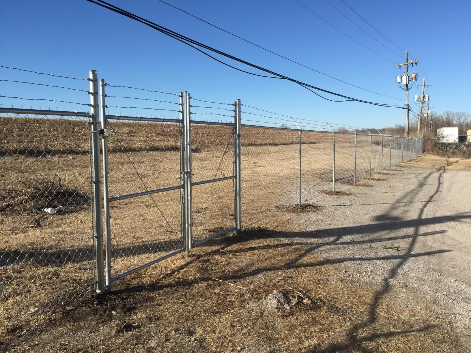 A chain link fence with barbed wire along the side of a dirt road.