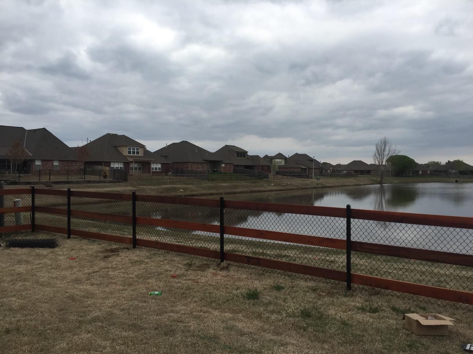 A wooden fence surrounds a lake with houses in the background