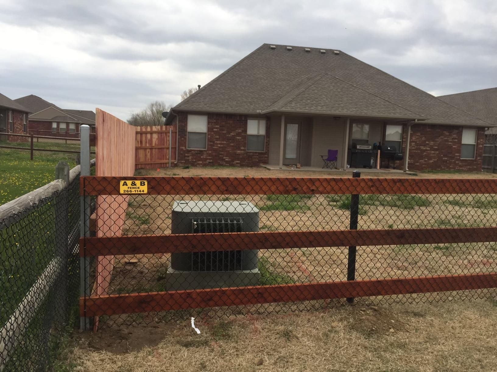 A wooden fence surrounds a chain link fence in front of a house.