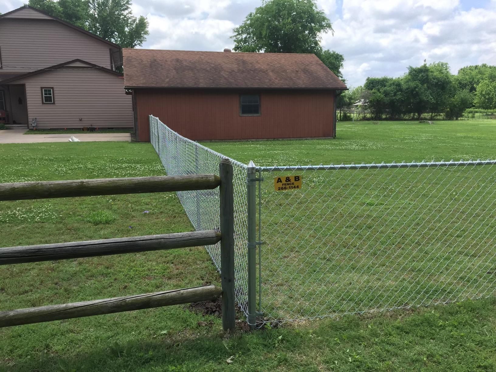 A chain link fence with a wooden fence in front of a house.