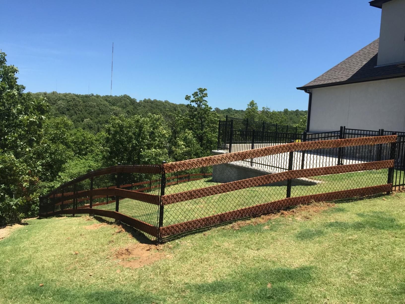 A wooden fence surrounds a lush green field in front of a house.