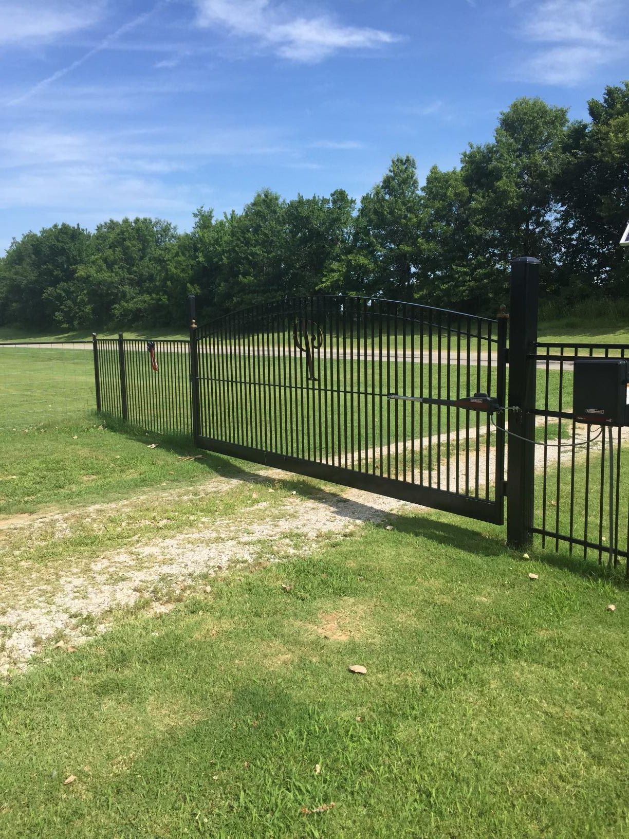 A fence surrounds a grassy field with trees in the background.