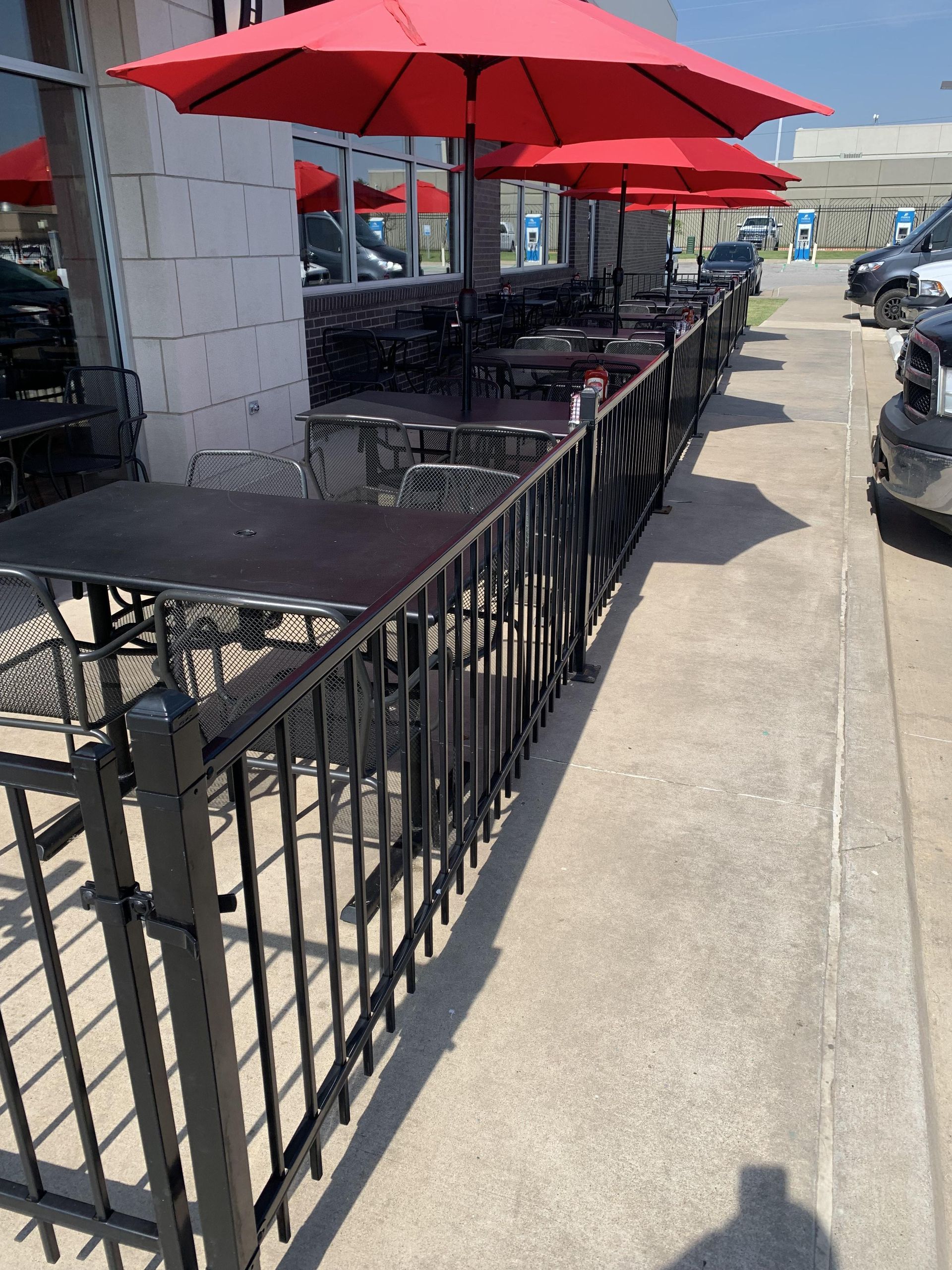 A row of tables and chairs with red umbrellas in a parking lot