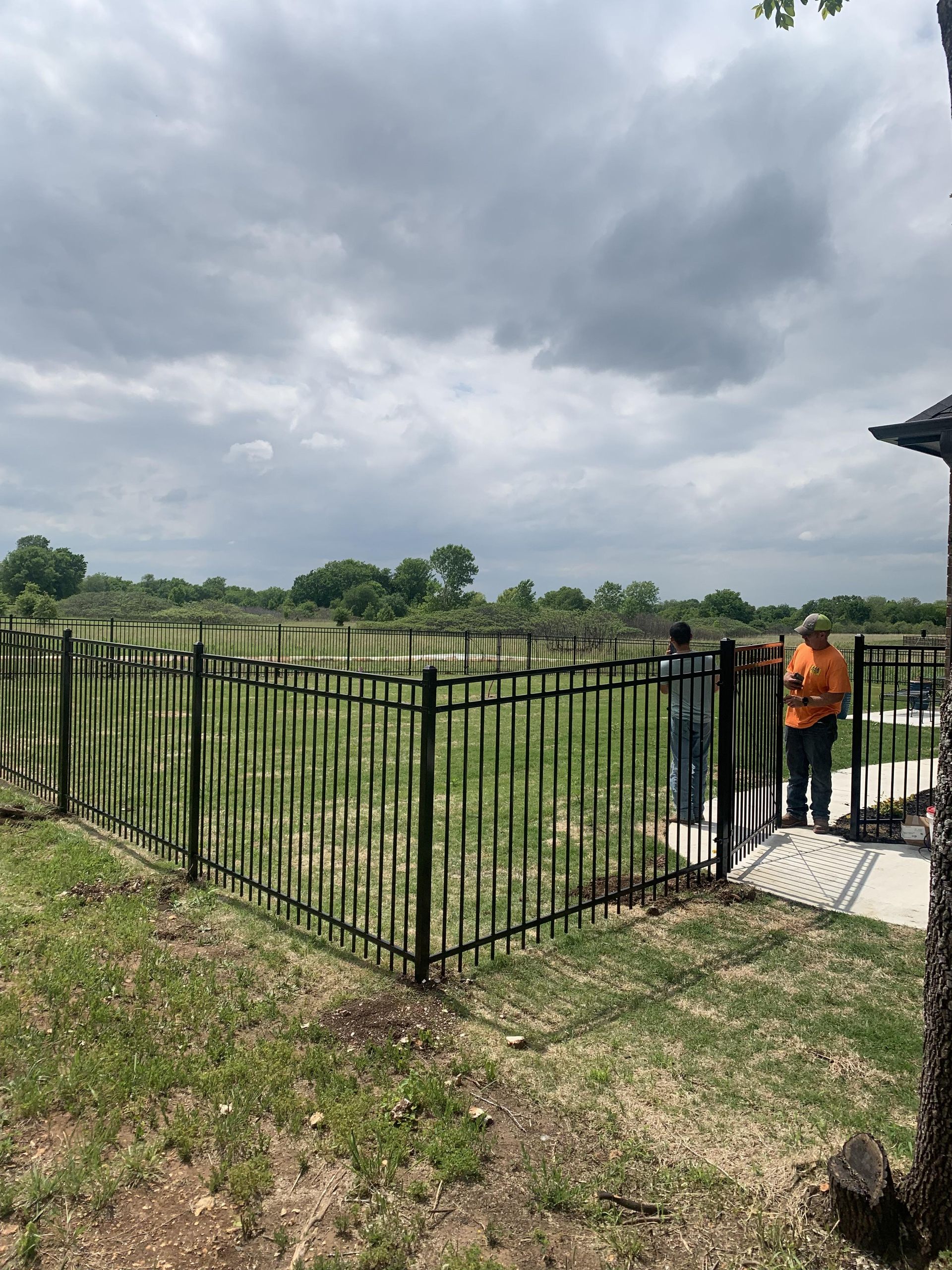 A couple of people standing next to a fence in a field.