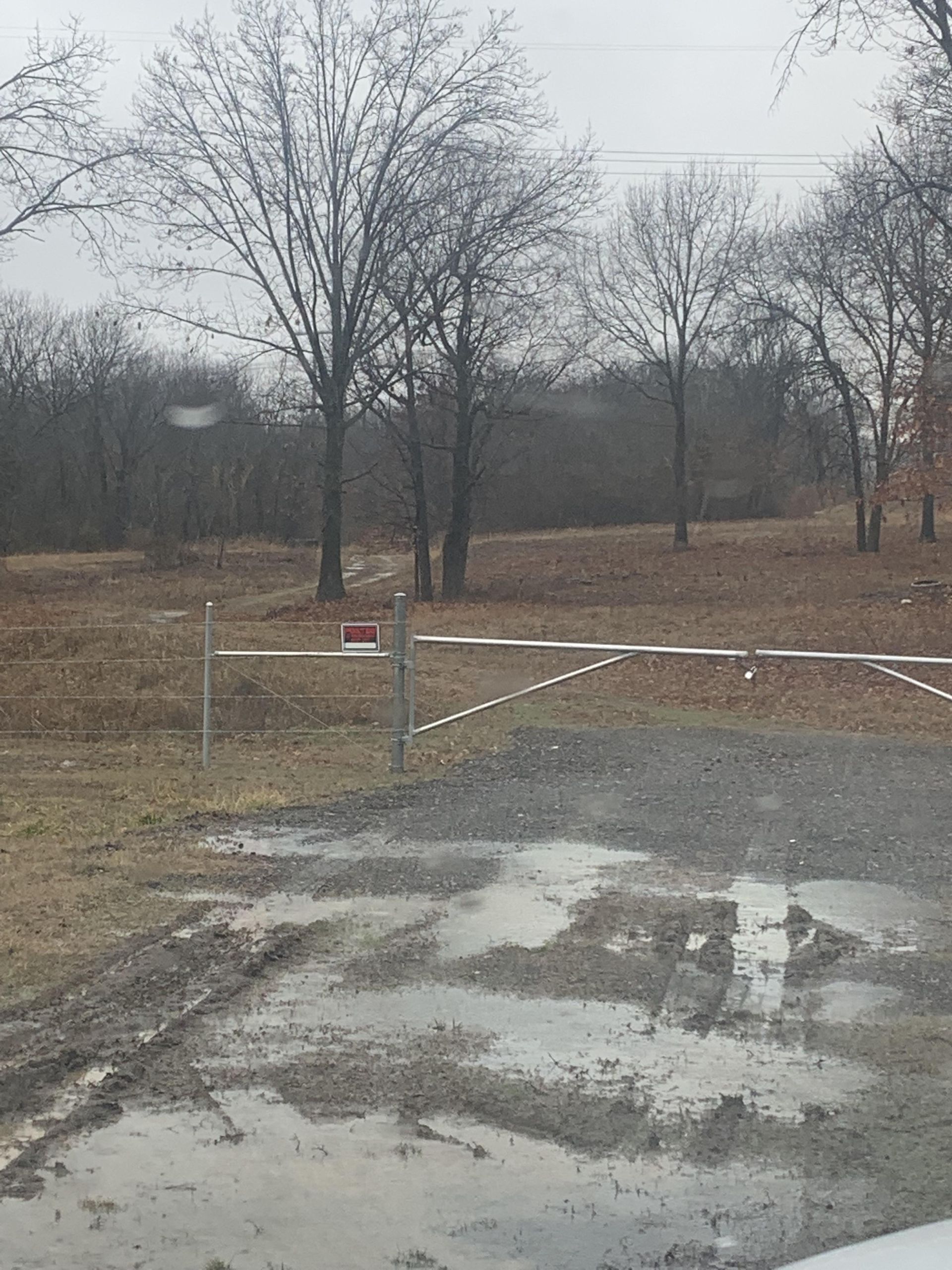 A muddy road with a fence and trees in the background