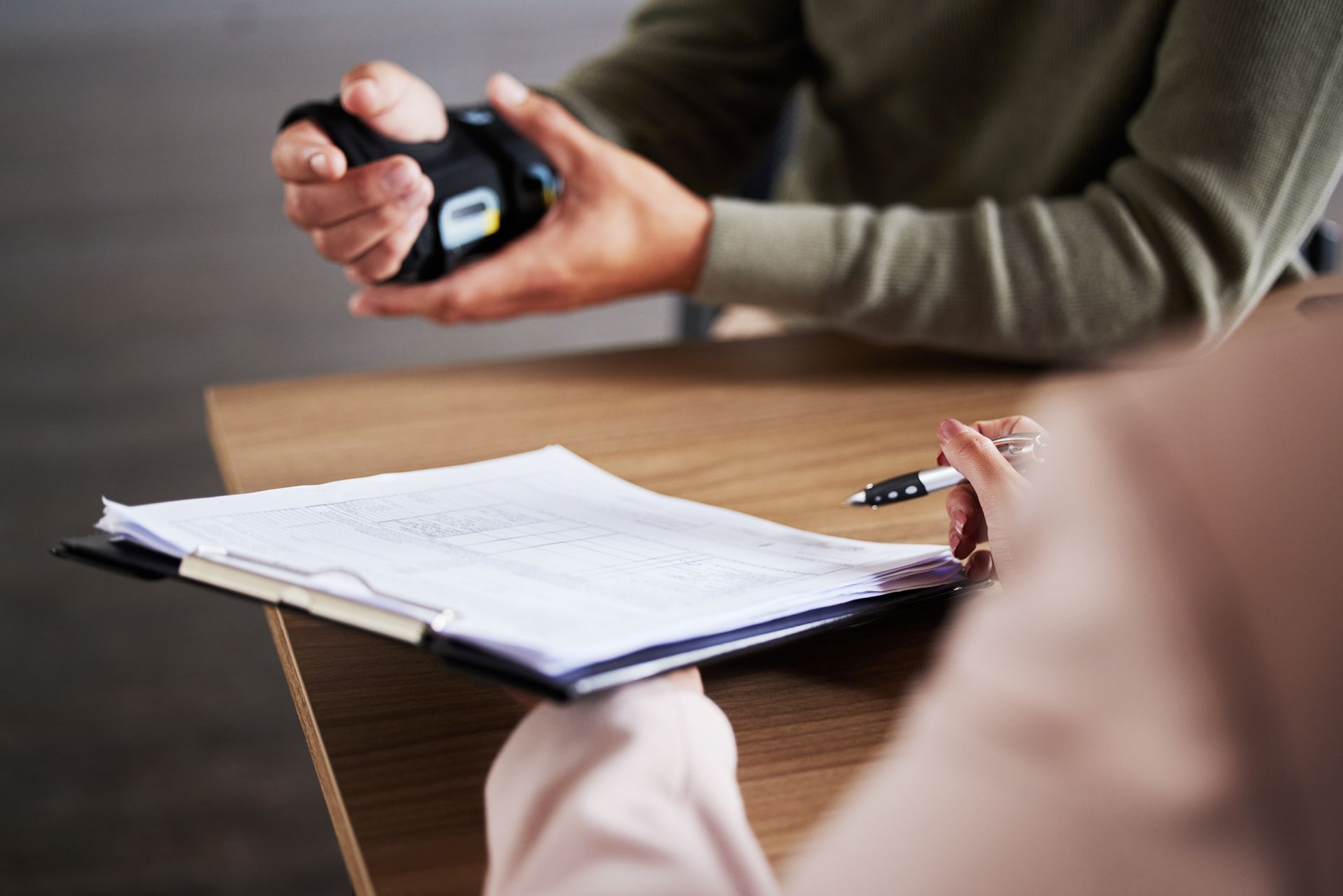 Close-up of people reviewing documents at table with pen and handheld device during business meeting.