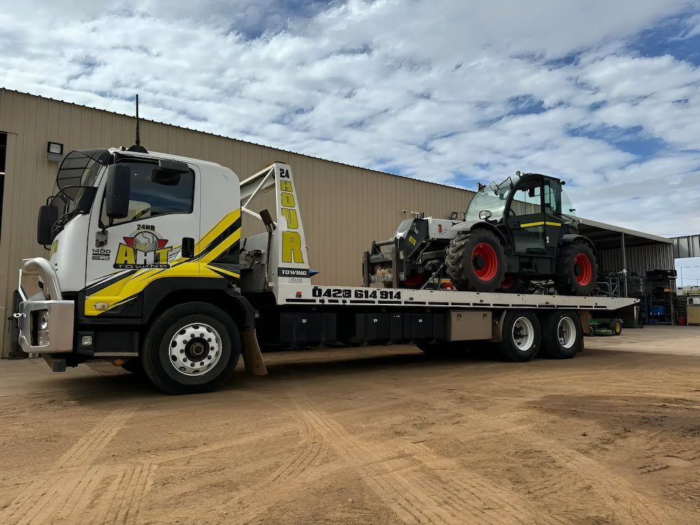 A Tow Truck With A Tractor On The Back Is Parked In Front Of A Building — AHT Towing in Ciccone, NT