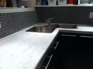 A kitchen with a stainless steel sink and black cabinets.