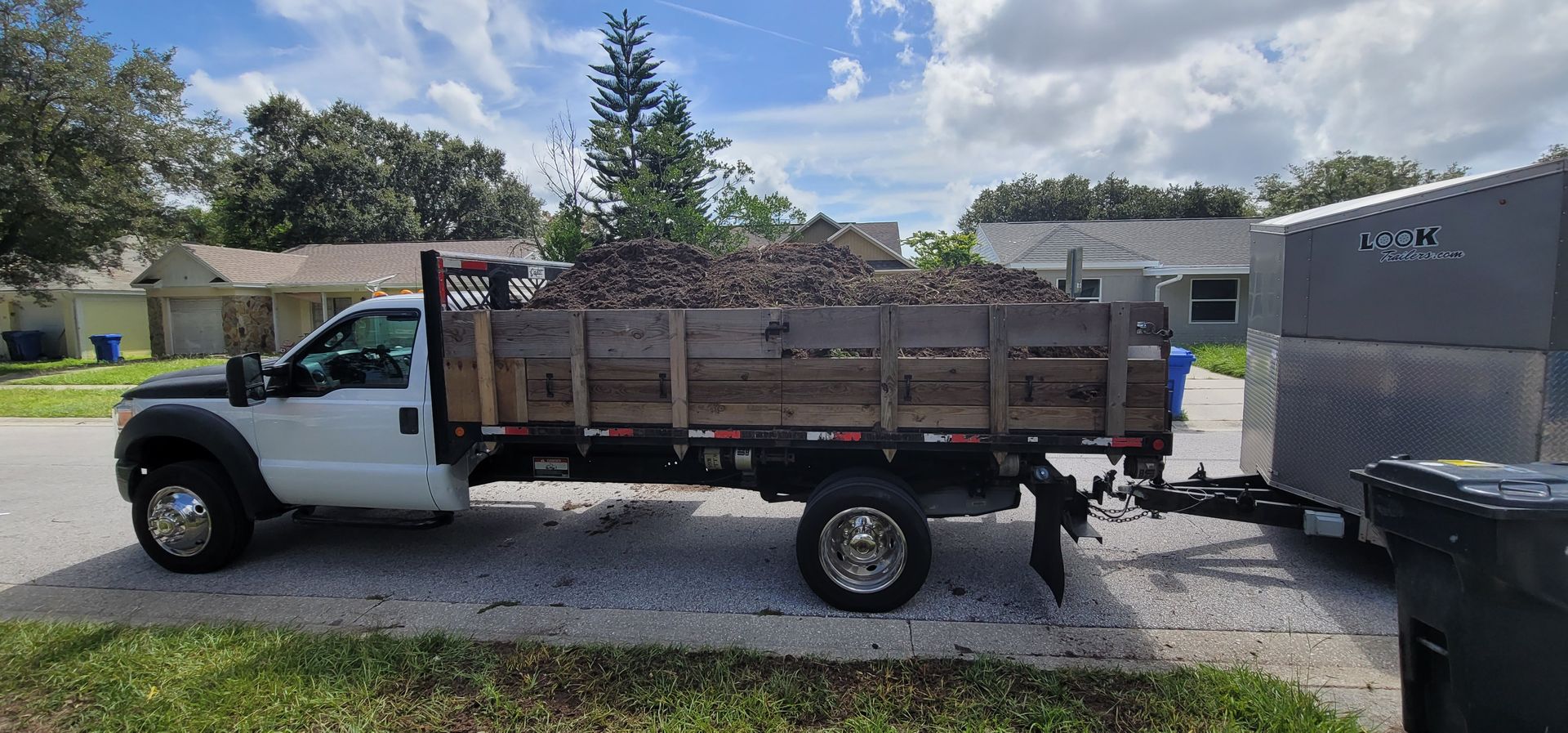 A dump truck with a trailer attached to it is parked on the side of the road filled with stump grindings.