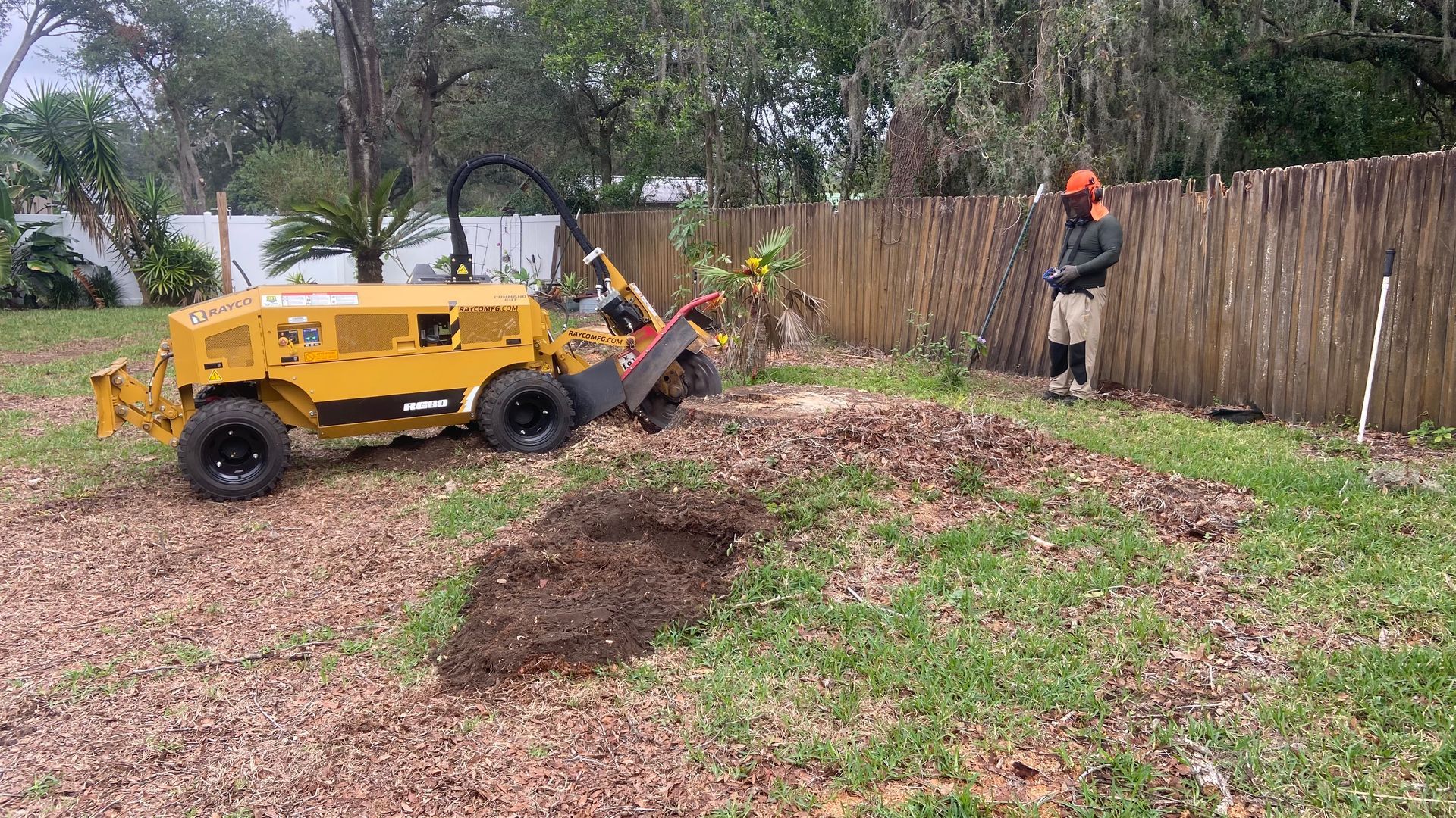 A man is standing next to a stump grinder in a yard.