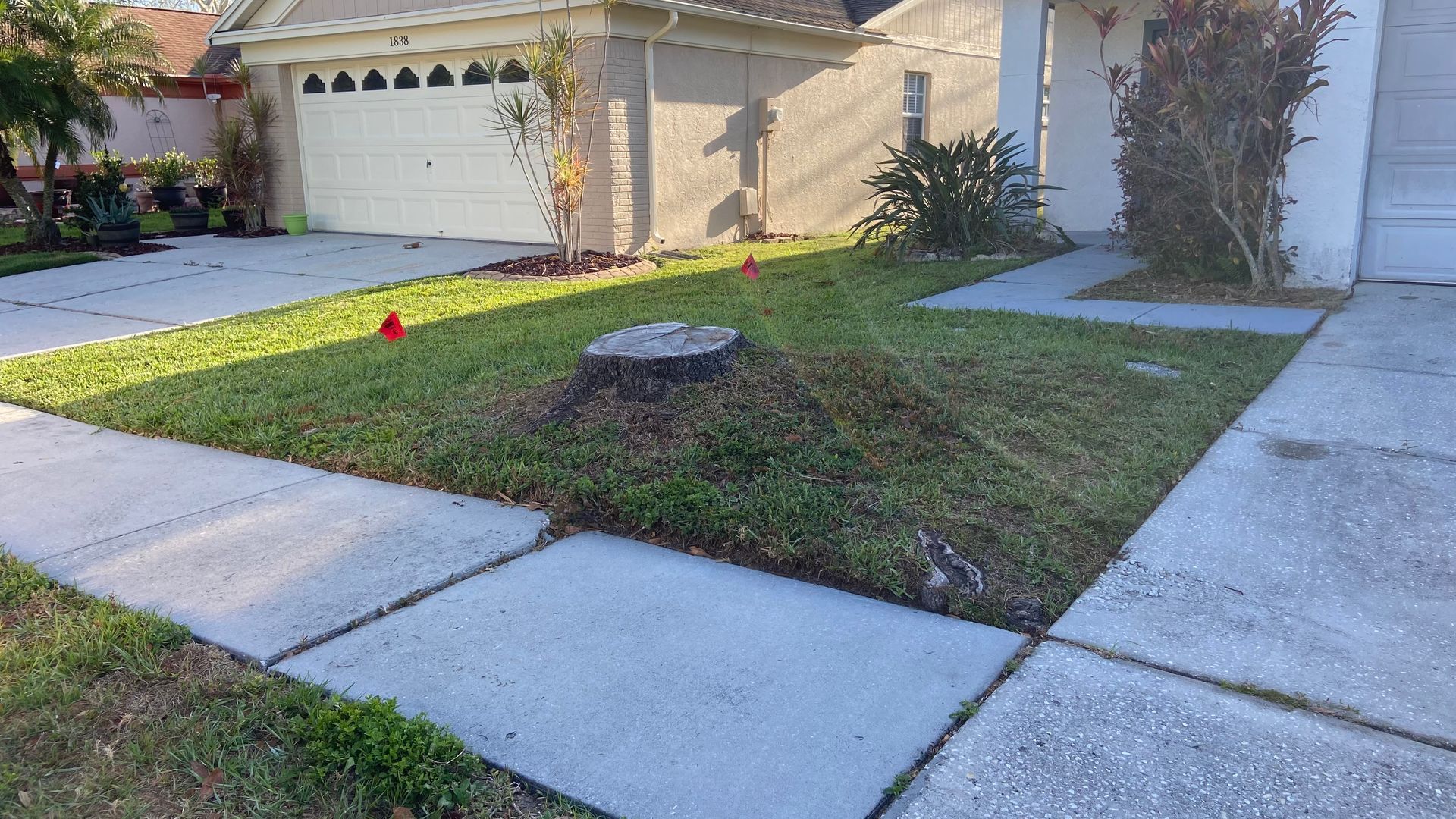 A stump in the middle of a lawn in front of a house.