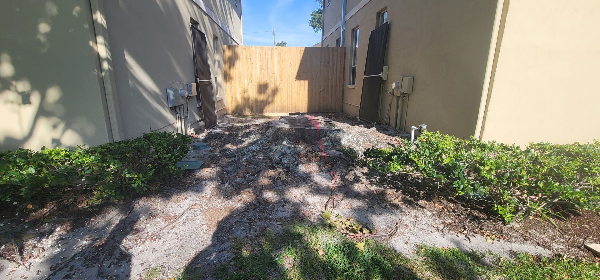 There is a wooden fence in the backyard of a house beside a stump.