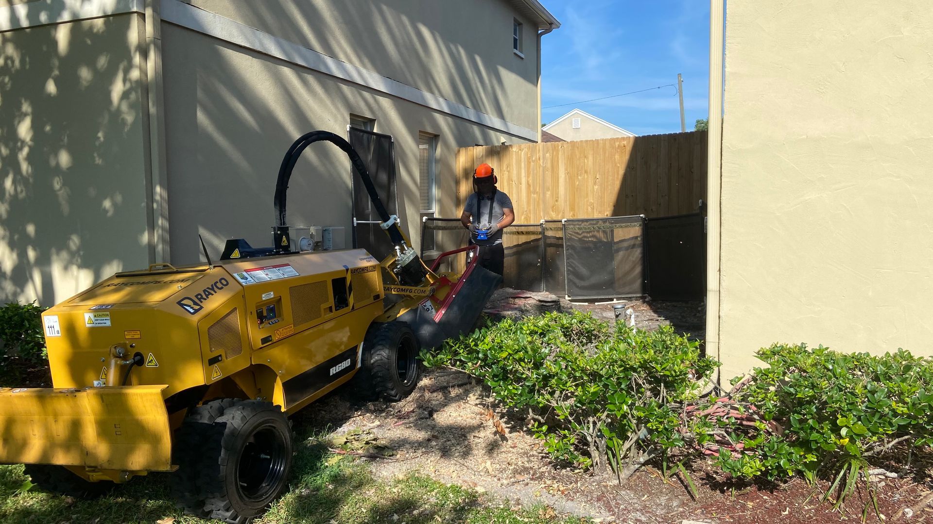 A man is working on a tree stump grinder in front of a house.