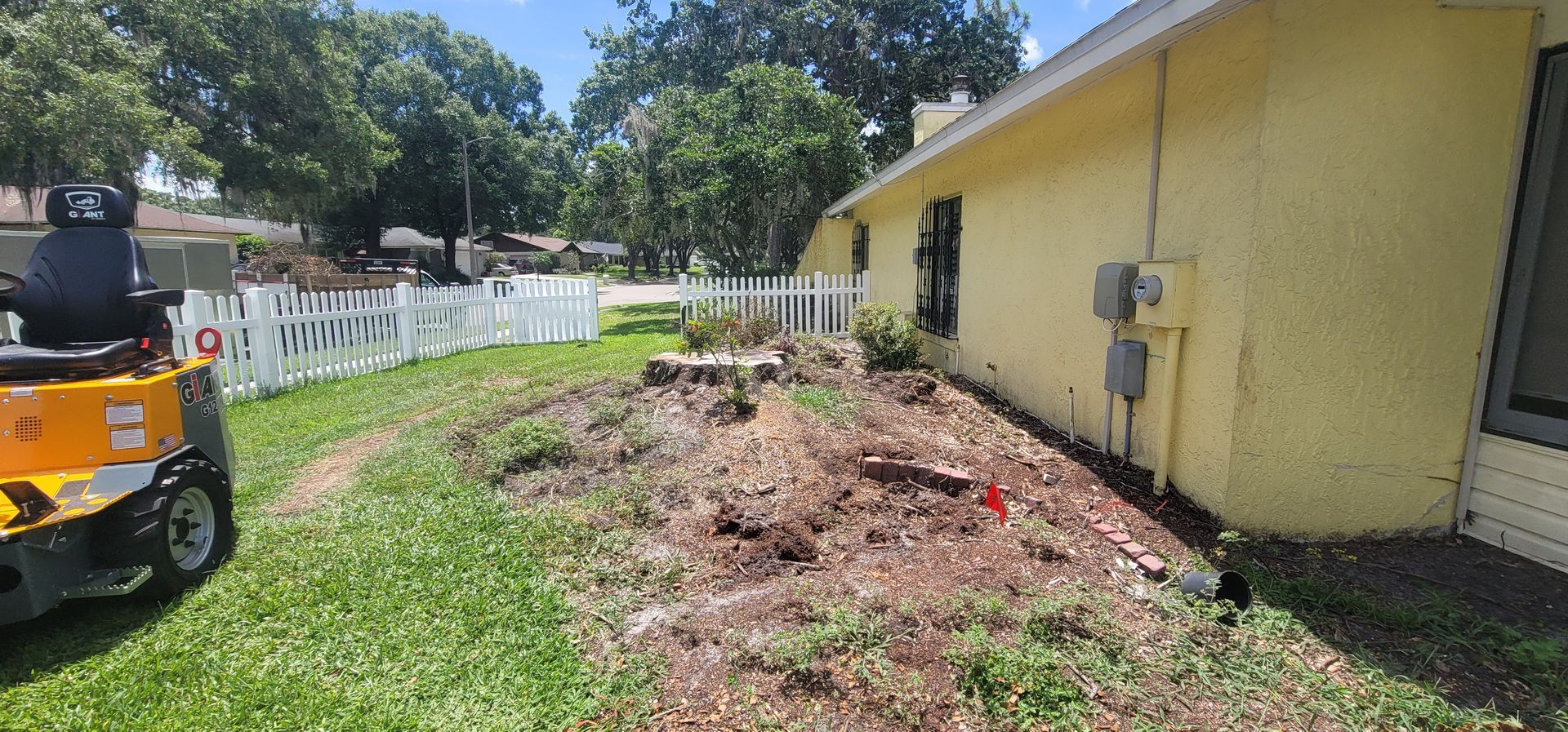 A yellow stump grinder is parked in front of a house.