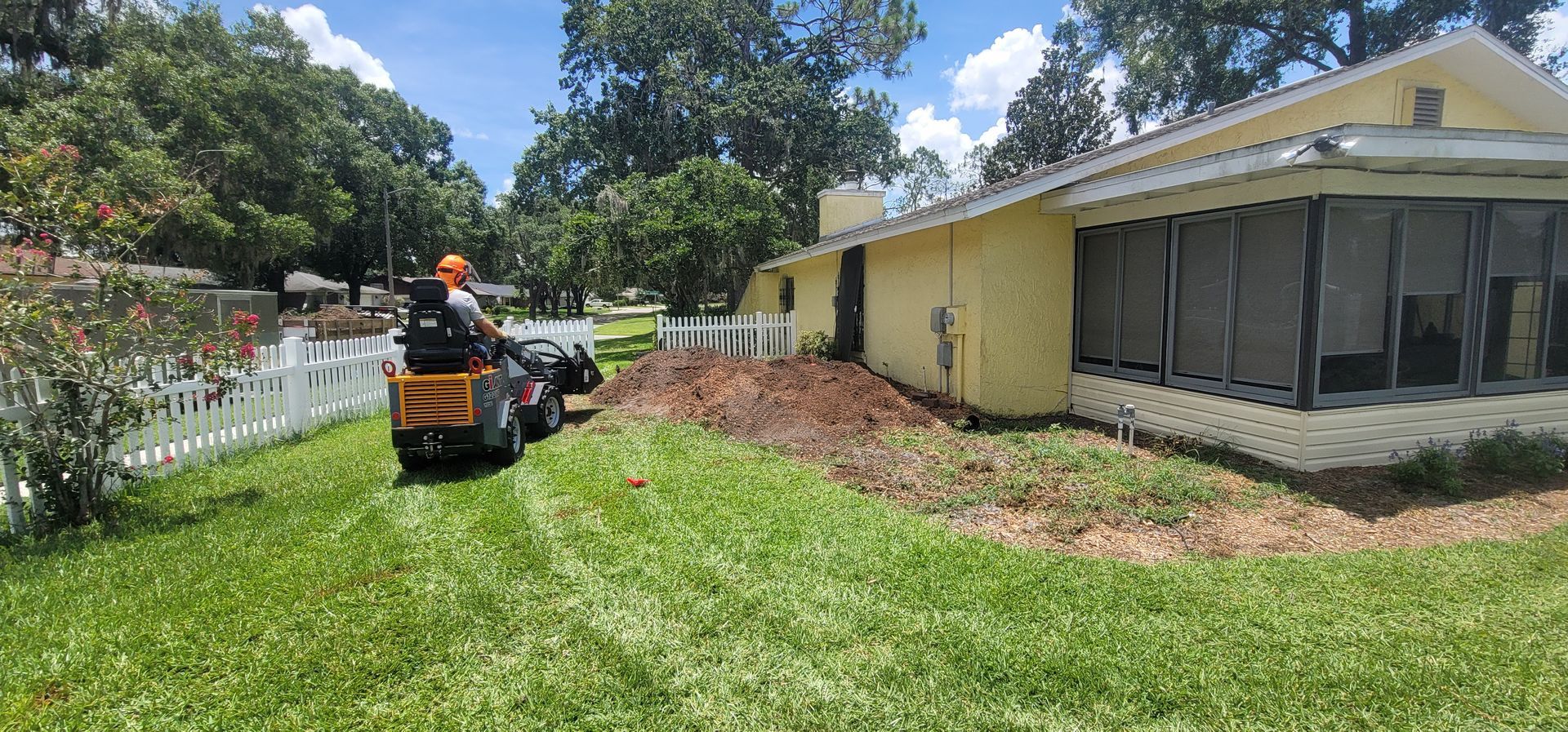 A man is driving a stump grinder in a yard in front of a house.