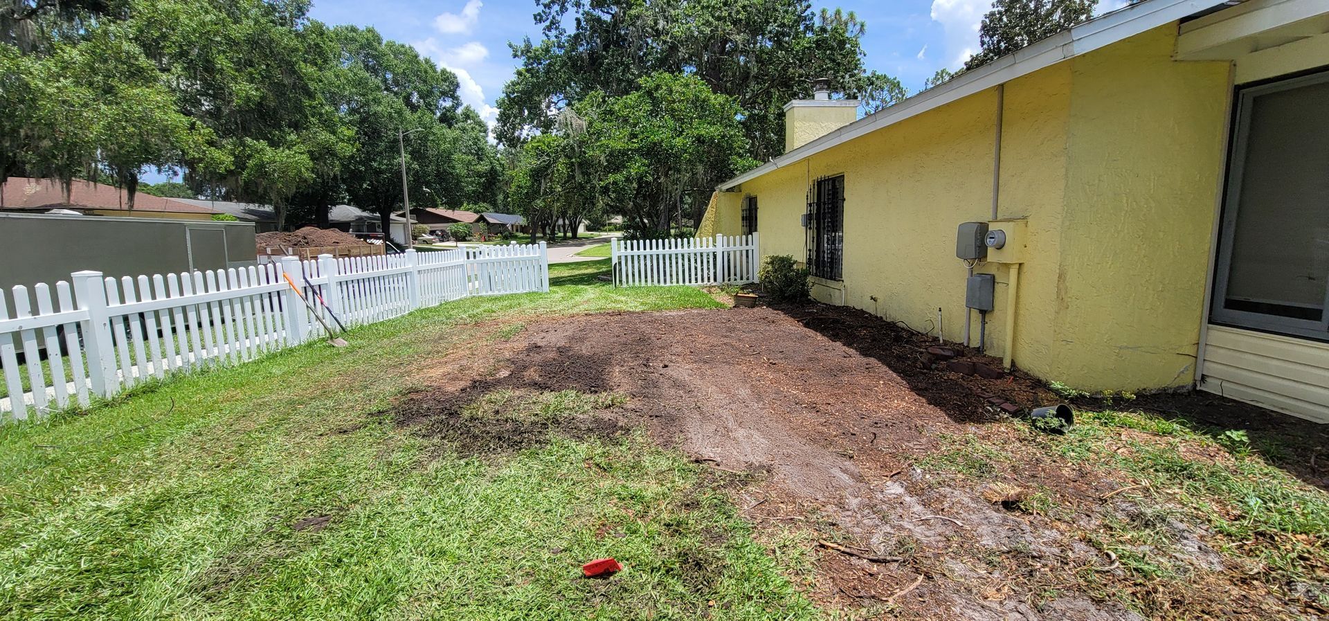 A yellow house with a white picket fence and dirt in front of it.