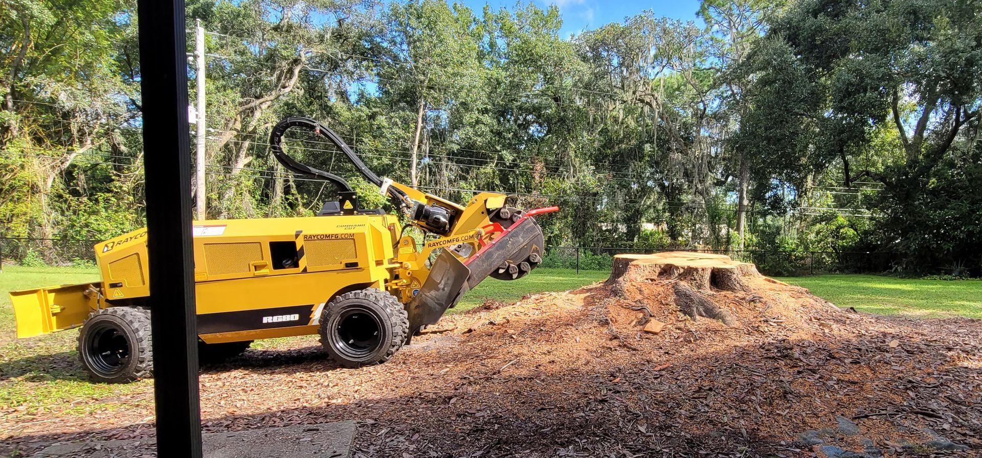 A yellow tractor is cutting a tree stump in a yard.