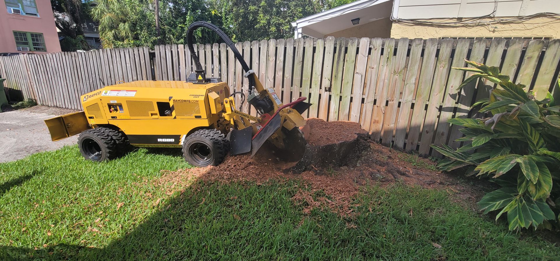 A yellow tractor is stump grinding a tree in a yard.