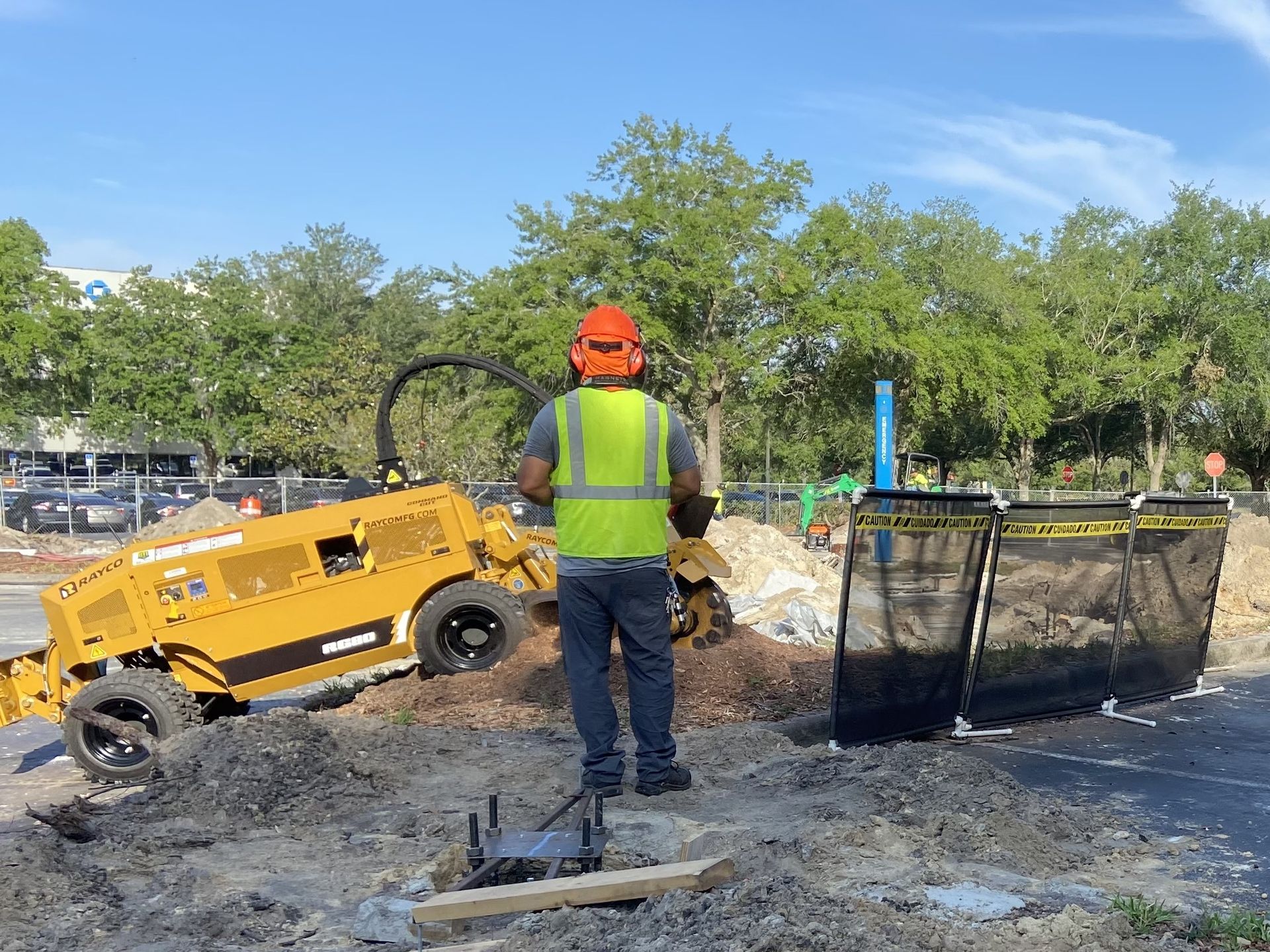 A construction worker is standing in front of a stump grinder.