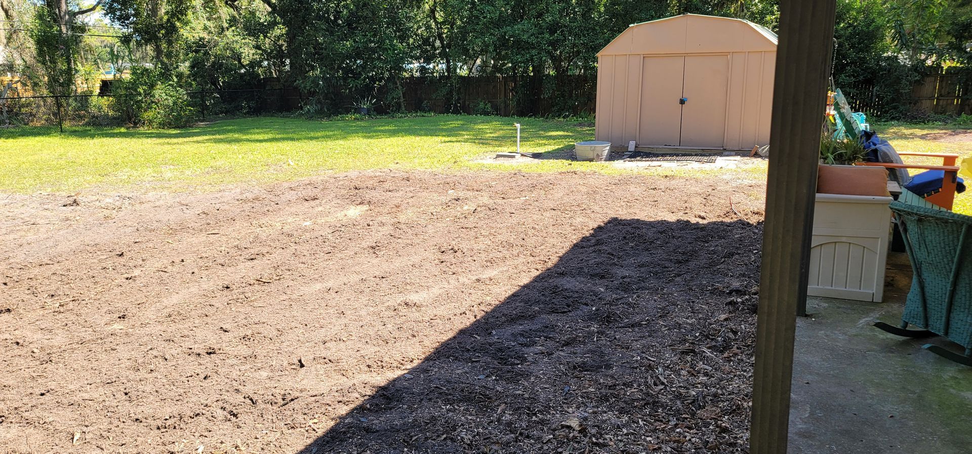 A shed is sitting in the middle of a dirt field in a backyard.