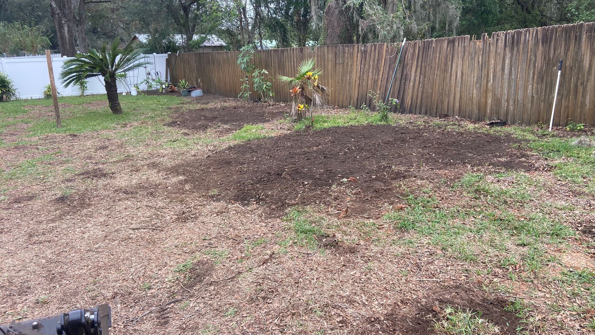 A backyard with a wooden fence and a pile of mulch.