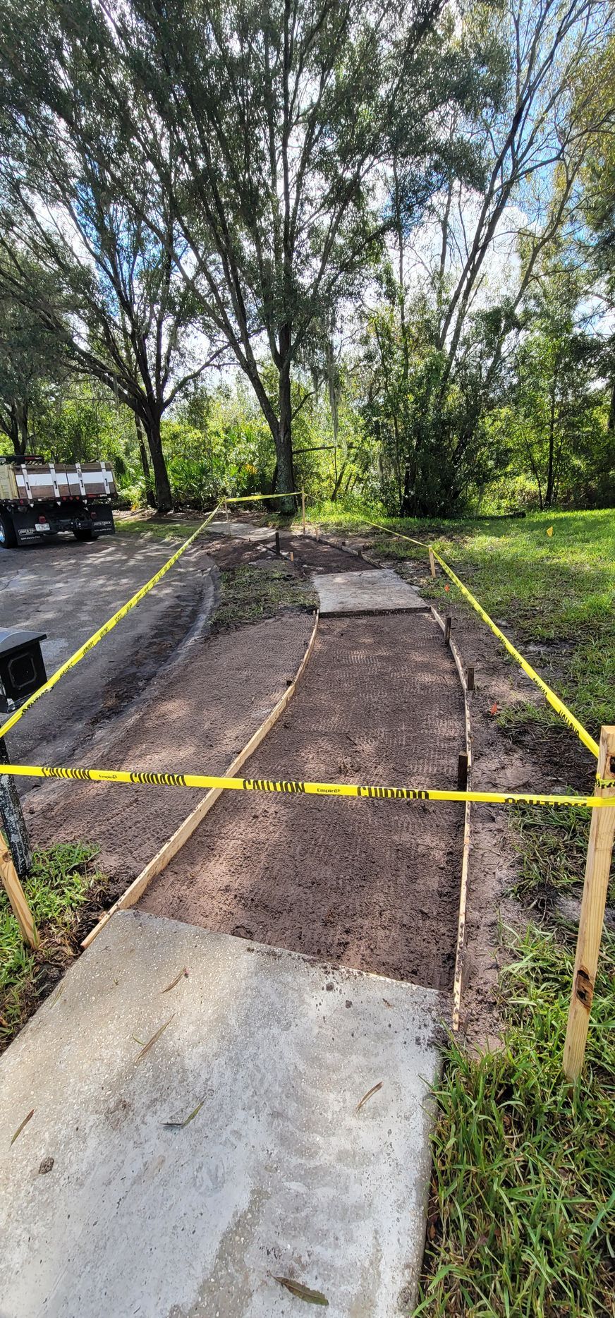 A concrete walkway is being built in a yard with trees in the background.