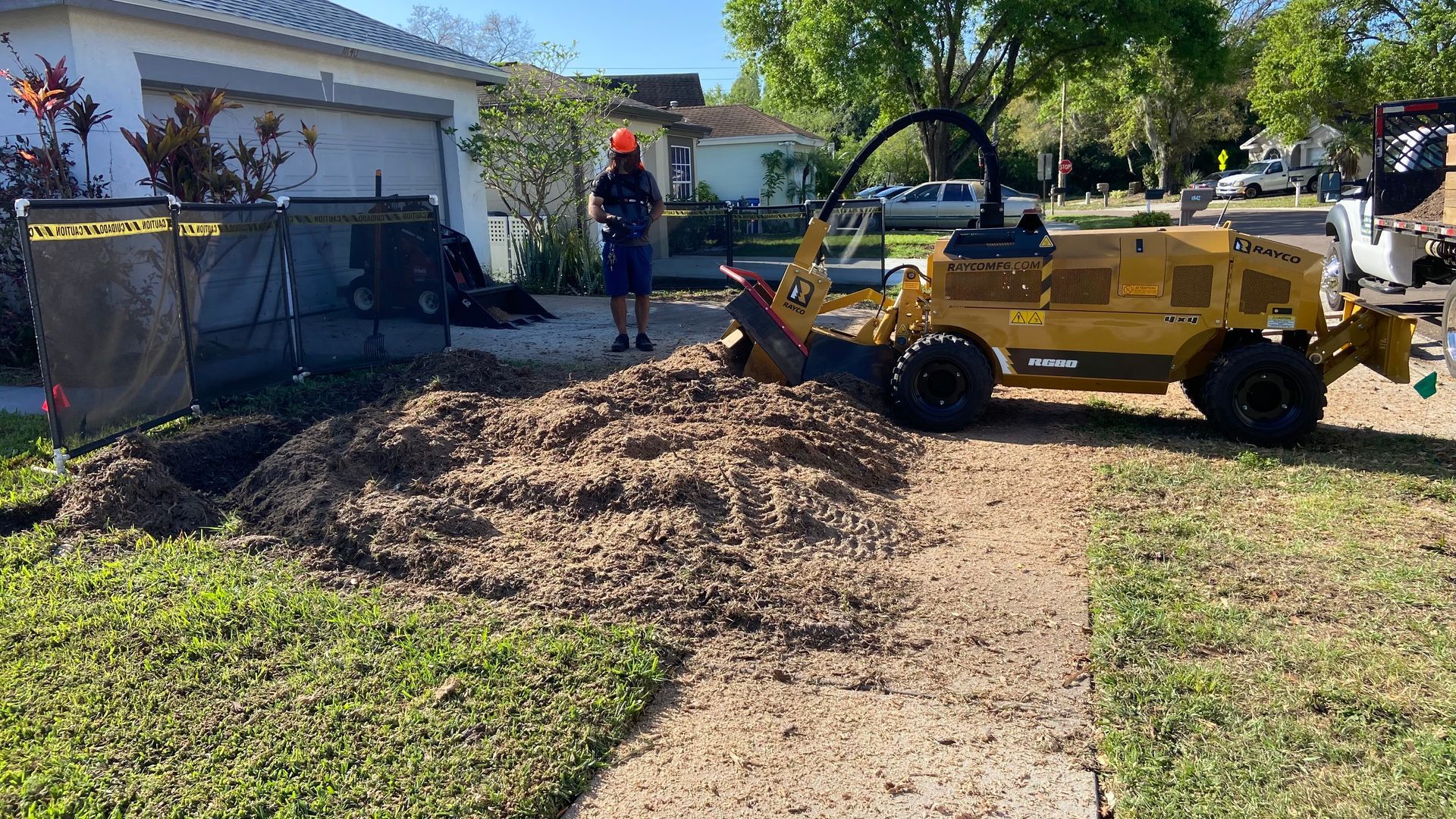 A man is standing next to a stump grinder in front of a house.