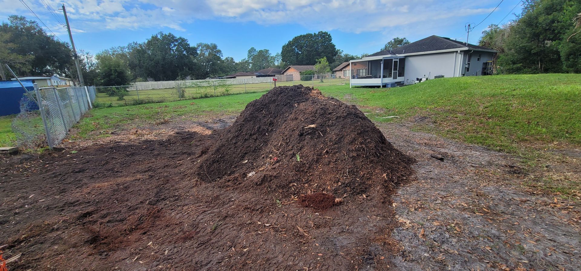 A pile of dirt is sitting on the side of a dirt road in front of a house.