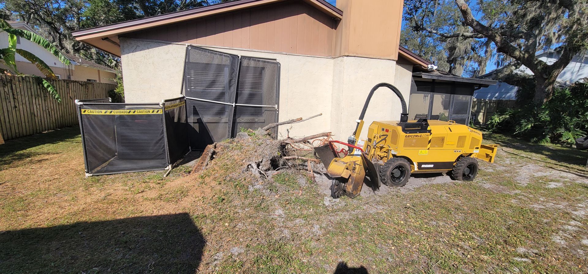 A yellow stump grinder is sitting in front of a house.