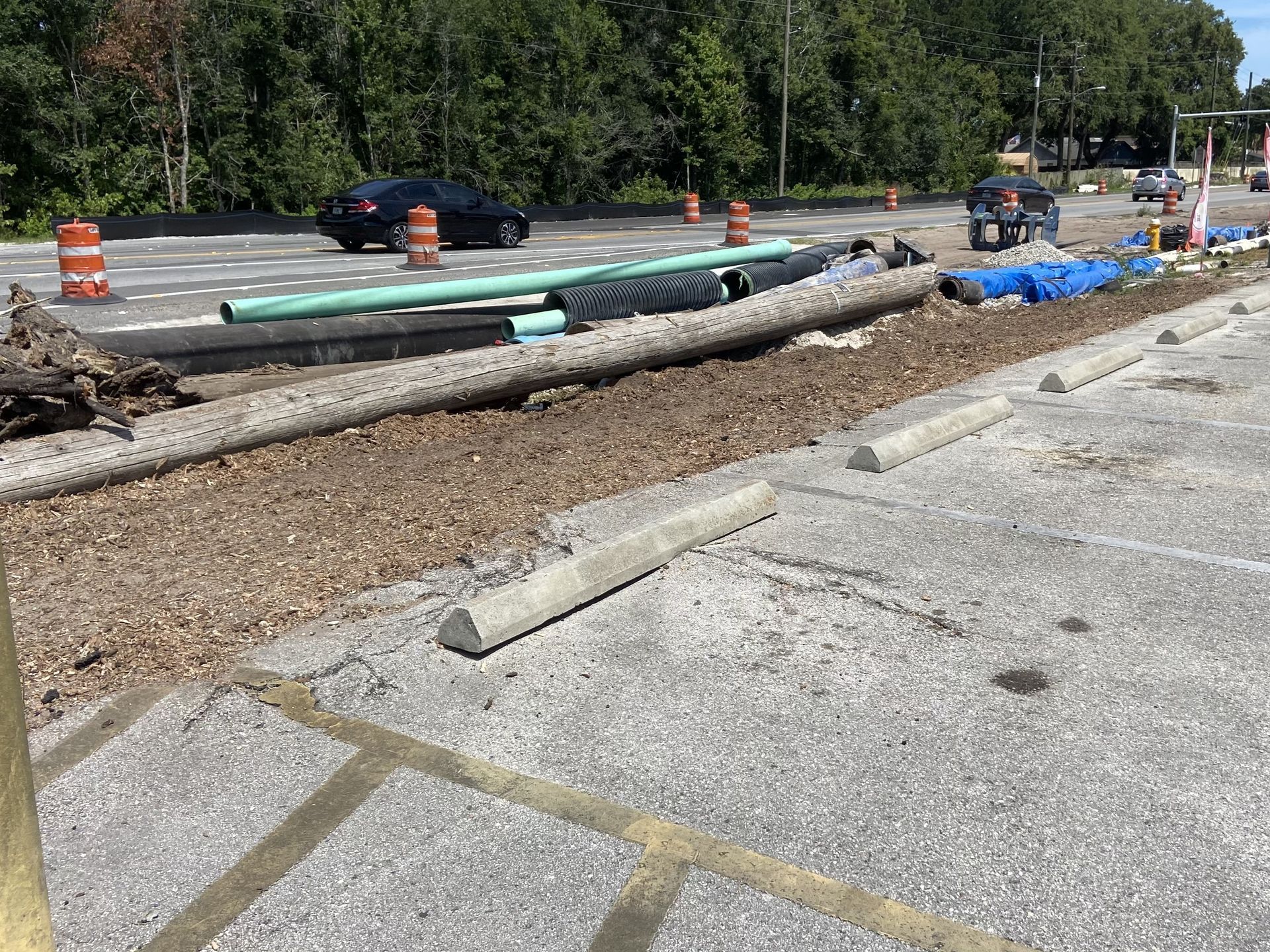 A lot of pipes are laying on the ground in a parking lot.