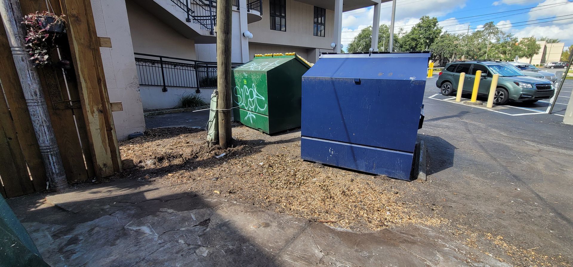 A blue trash can is sitting next to a green trash can in a parking lot.