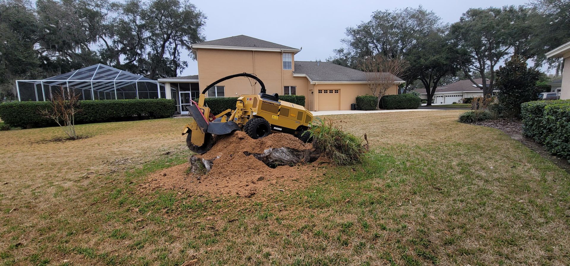 A stump grinder is sitting in the grass in front of a house.