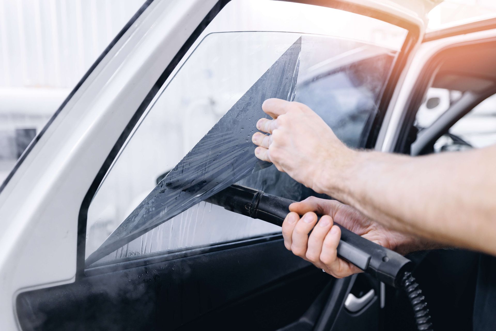 A man is cleaning a car window with a steam cleaner.