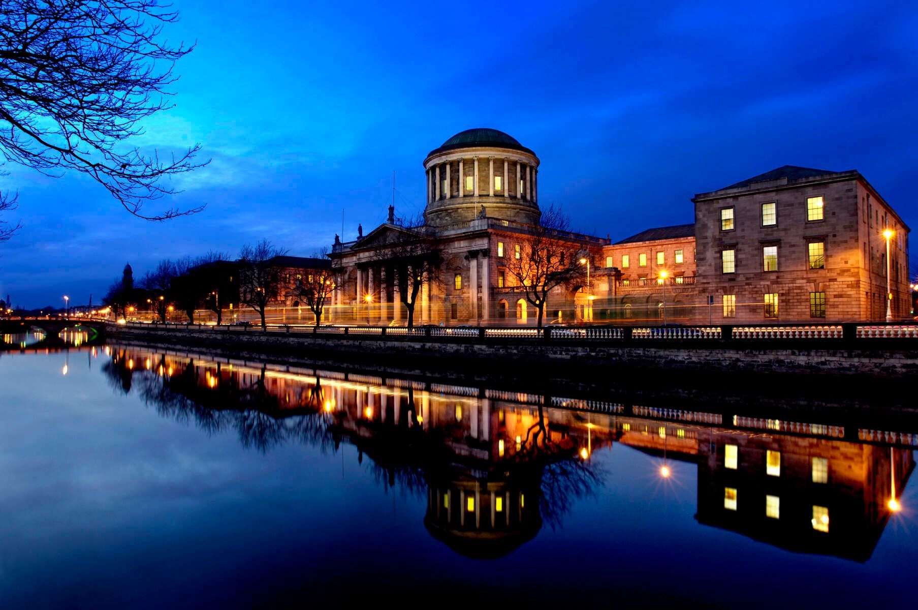 Courthouse lit up at night, reflecting in calm water, along a river.