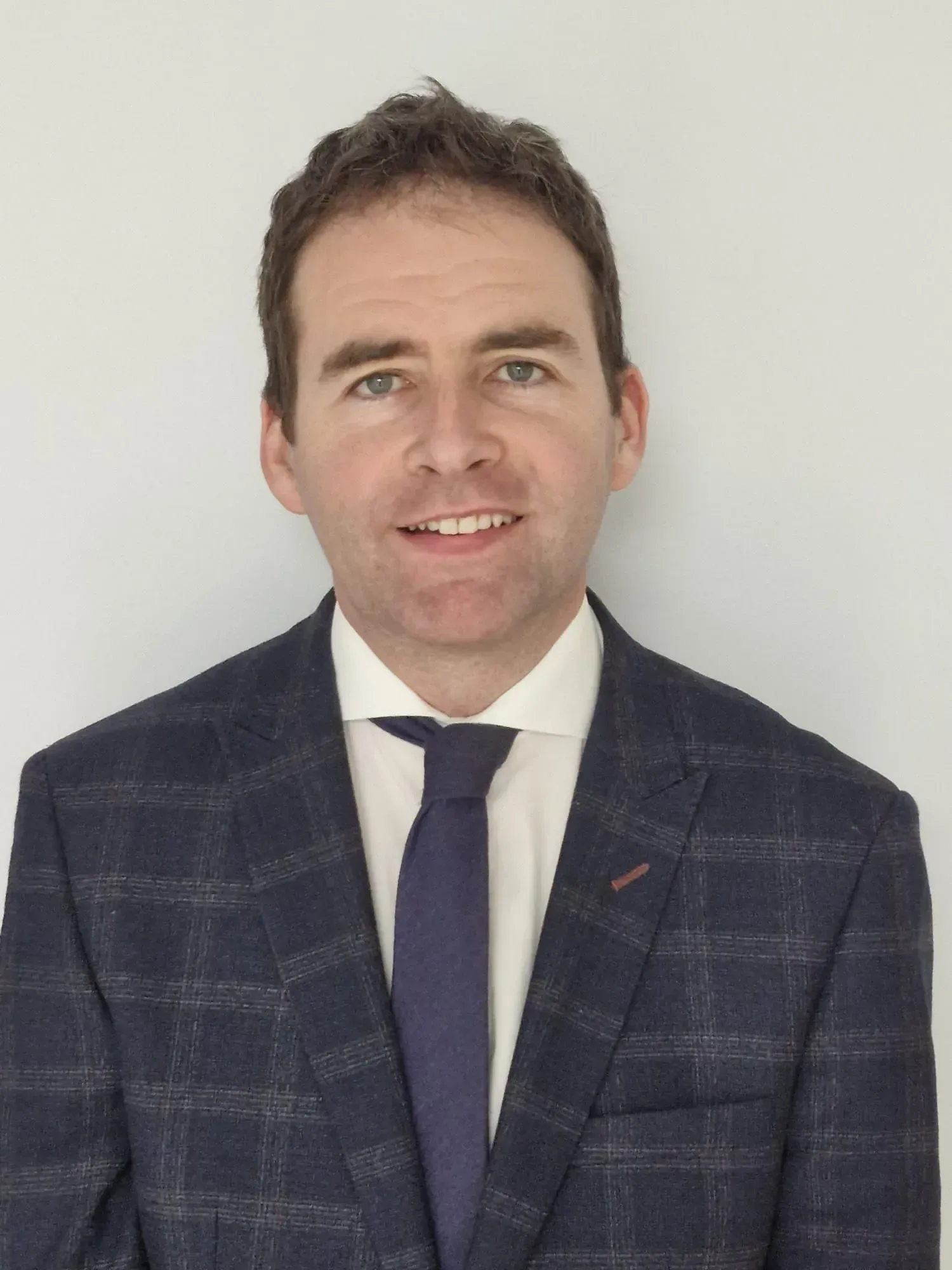 Man in suit, smiling, standing in front of a white wall.