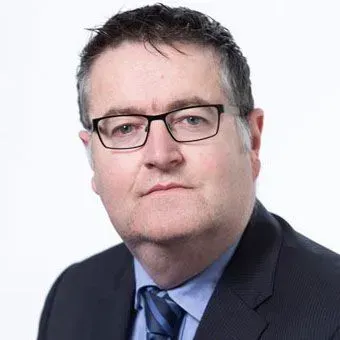 Man with glasses and dark suit, looking at the viewer.