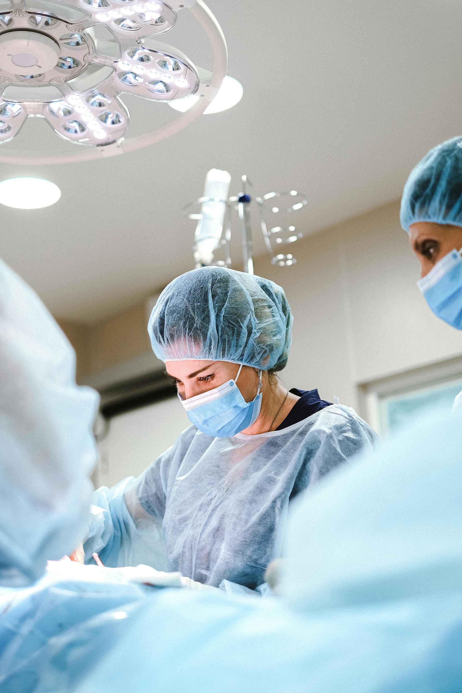 Surgeon in blue scrubs and mask operating in a bright operating room.