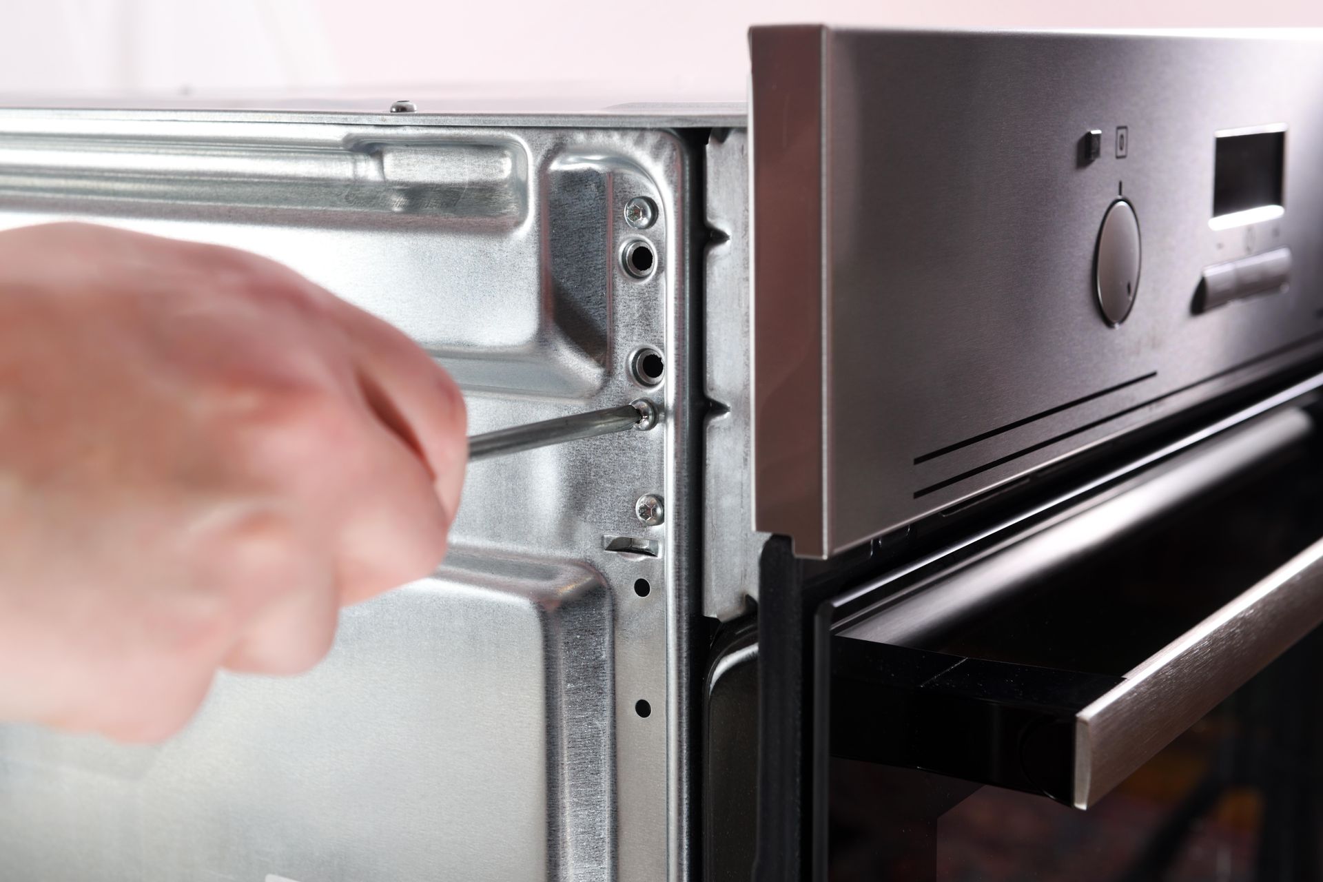 Person Using a Screwdriver to Remove Screws From an Oven — Mazlin Electrical Services Pty Ltd in Annandale, QLD