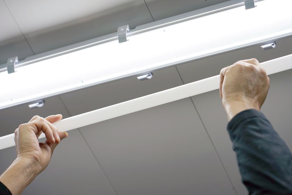 Hands Installing a Long, White Light Fixture to a Ceiling — Mazlin Electrical Services Pty Ltd in Mount Low, QLD