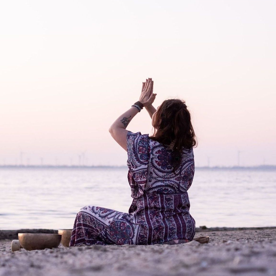 Handen houden een witte kop warme chocolademelk vast op een houten tafel, met cacaonibs ernaast.