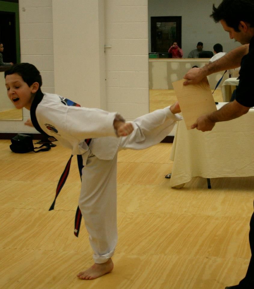 Two people grappling on a mat, one in a black gi, the other in a rash guard, legs entangled.